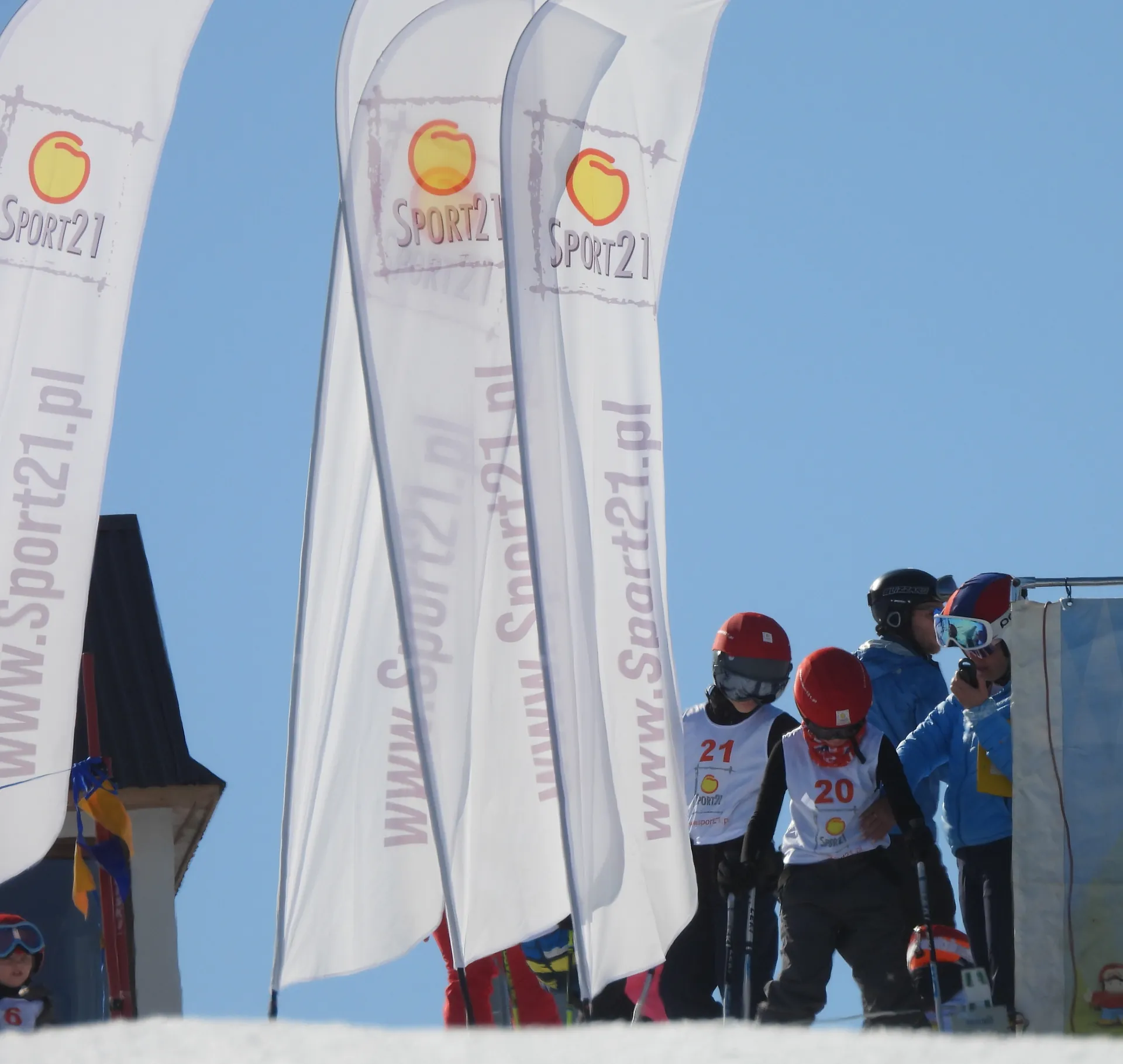 Młodzi narciarze przy flagach Sport21 na stoku